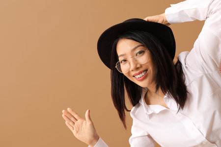 Beautiful young Asian woman waving hand on beige backgroundの写真素材
