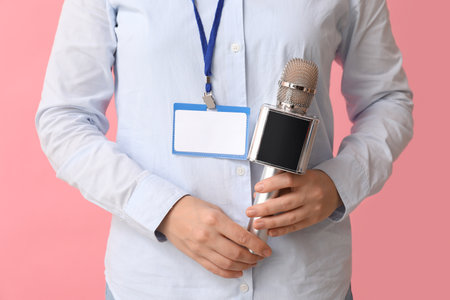 Female journalist with microphone and blank ID badge on pink background, closeupの写真素材