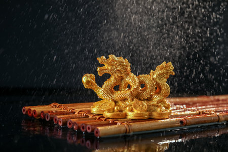 Golden Chinese dragon figurine on bamboo mat under falling water droplets against black background. New Year celebrationの写真素材
