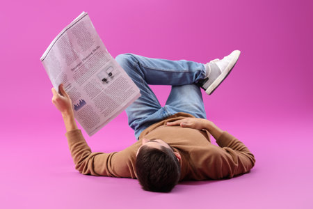 Young man with newspaper lying on purple backgroundの写真素材