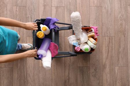 Female janitor with trolley of cleaning supplies on wooden floor, top viewの写真素材