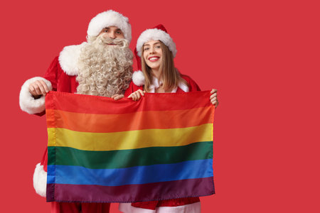 Young couple dressed as Santa Clauses with LGBT flag on red backgroundの写真素材