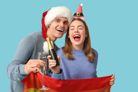 Young couple in Santa hats with LGBT flag and champagne on blue backgroundの写真素材