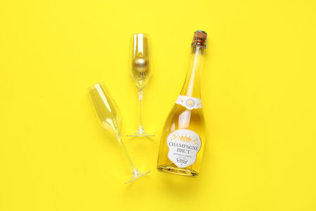 Bottle of champagne and glasses with Christmas ball on yellow backgroundの写真素材