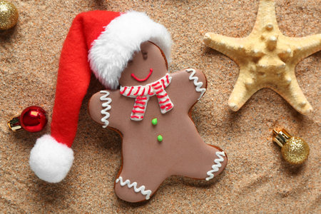 Tasty gingerbread cookie with starfish and Christmas decor on sand background