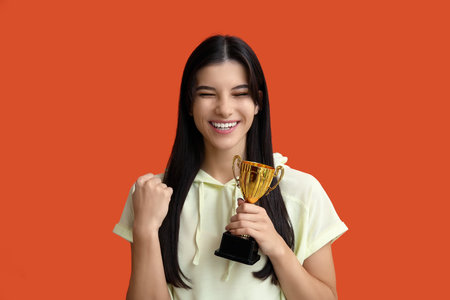 Sporty young woman with gold cup on orange backgroundの写真素材