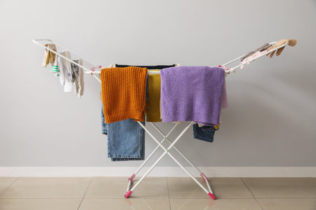 Clean winter clothes hanging on dryer near light wall