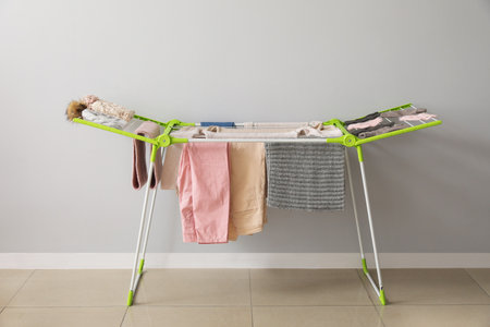 Clean winter clothes hanging on dryer near light wallの写真素材