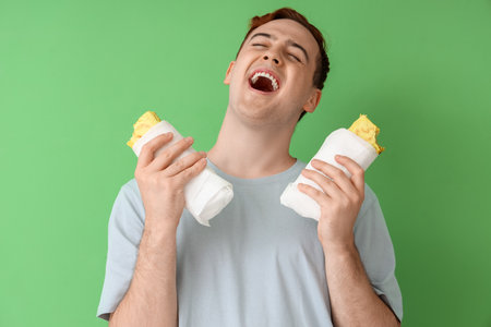 Happy young man with tasty sandwich wraps on green background, closeupの写真素材