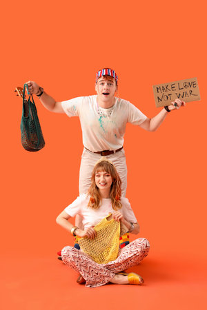 Couple of hippies with string bags and placard on orange backgroundの写真素材