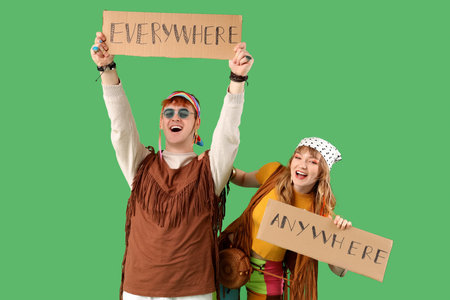 Couple of hippies holding cardboard sheets with words EVERYWHERE and ANYWHERE on green backgroundの写真素材