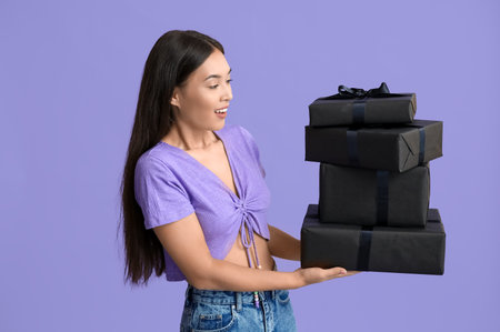 Beautiful young Asian woman with gift boxes on purple background. Black Friday saleの写真素材