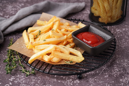 Grid with tasty French fries and ketchup on gray background