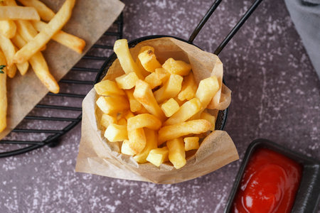 Deep fryer basket with French fries and ketchup on gray background