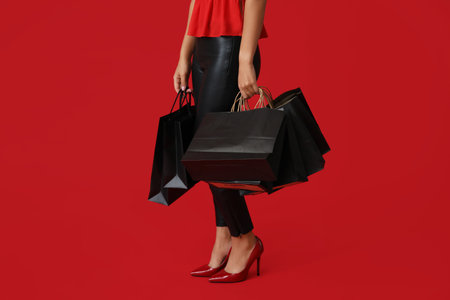 Beautiful young Asian woman with shopping bags on red background, closeup. Black Friday saleの写真素材