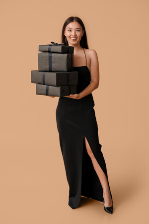 Beautiful young Asian woman with gift boxes on brown background. Black Friday saleの写真素材