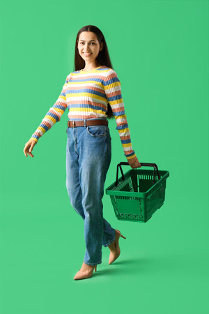 Young woman with shopping basket on green backgroundの写真素材