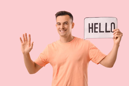 Handsome man holding paper speech bubble with word HELLO on pink background