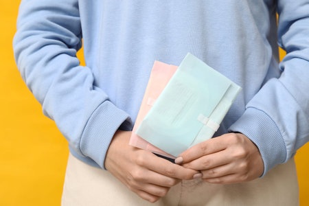 Beautiful young woman with menstrual pads on yellow background, closeup