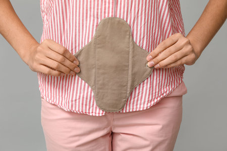 Beautiful young woman with reusable menstrual pad on gray background, closeupの写真素材