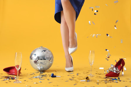 Young woman legs with disco ball and party decor on yellow background. New Year celebrationの写真素材