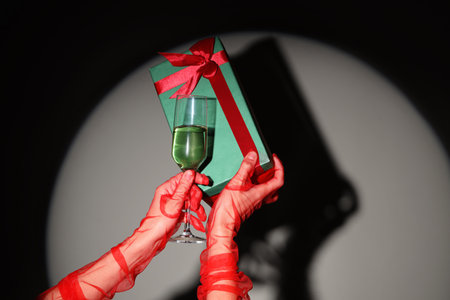 Female hand with glass of champagne and gift box on light backgroundの写真素材
