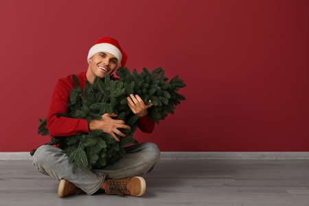 Young man in Santa hat with Christmas tree on red backgroundの写真素材