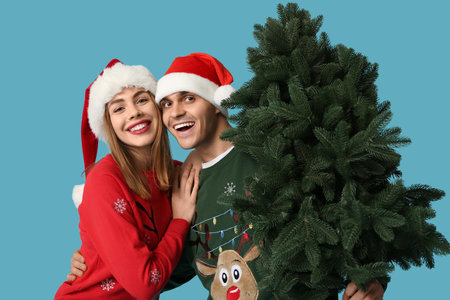 Happy young couple in Santa hats with Christmas tree on blue backgroundの写真素材