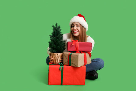 Beautiful young woman with Christmas tree and gift boxes on green background