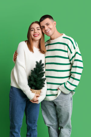 Beautiful young couple with Christmas tree on green backgroundの写真素材