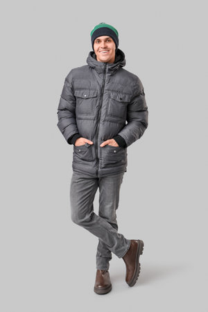 Young man in stylish puffer jacket and hat on gray backgroundの写真素材