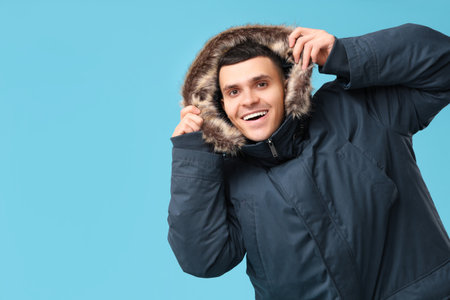 Young man in stylish puffer jacket on blue backgroundの写真素材
