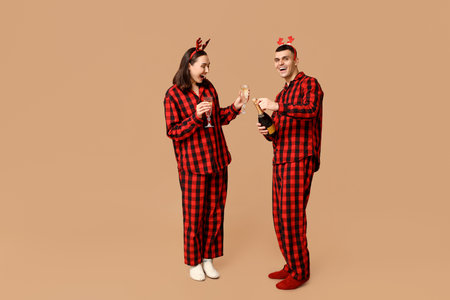Happy young couple in Christmas pajamas and with champagne on beige backgroundの写真素材