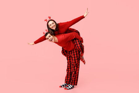 Happy young couple in Christmas pajamas having fun on pink backgroundの写真素材
