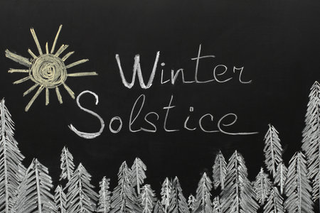 Text WINTER SOLSTICE with drawn sun and fir trees on dark backgroundの写真素材