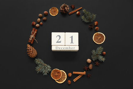 Calendar with date of winter solstice, fir branches, cinnamon, nuts and dried oranges on dark backgroundの写真素材