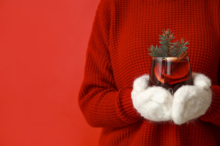 Young woman in warm mittens with glass of hot mulled wine on red backgroundの写真素材