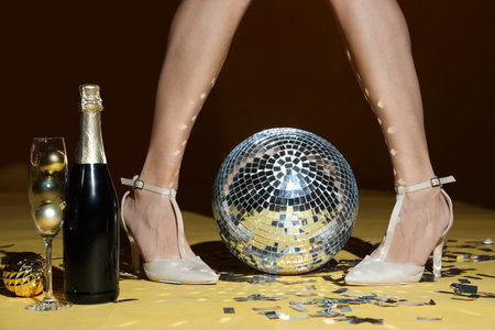Young woman legs with champagne, disco ball and party decor on yellow background. New Year celebrationの写真素材