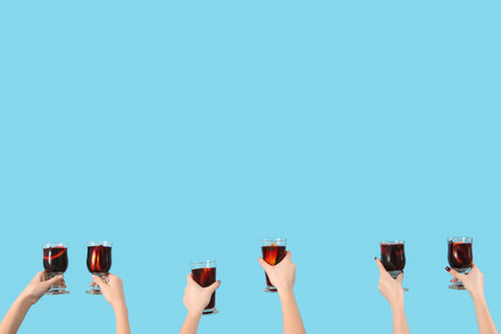 Female hands with glasses of warm mulled wine on blue backgroundの写真素材