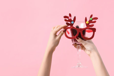 Female hands with glass of warm mulled wine and Christmas reindeer horns on pink backgroundの写真素材