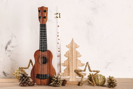Composition with ukulele, flute and Christmas decorations on wooden table against light backgroundの写真素材