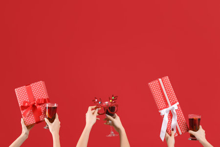 Female hands with glasses of warm mulled wine and gift boxes on red backgroundの写真素材