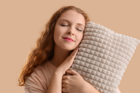 Beautiful young woman with soft pillow on beige backgroundの写真素材