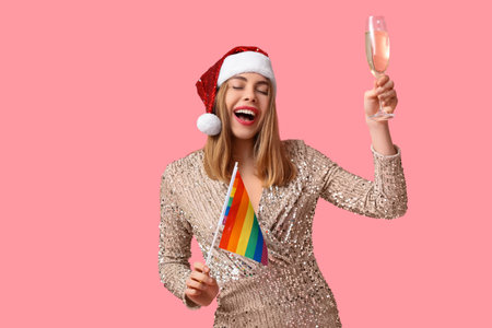 Young woman in Santa hat with LGBT flag and champagne on pink backgroundの写真素材