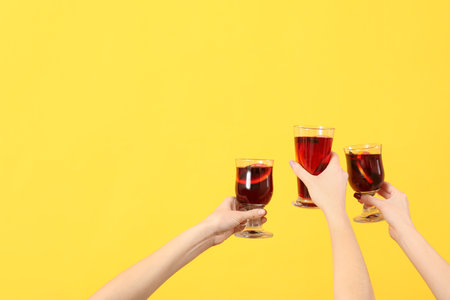 Female hands with glasses of warm mulled wine on yellow backgroundの写真素材