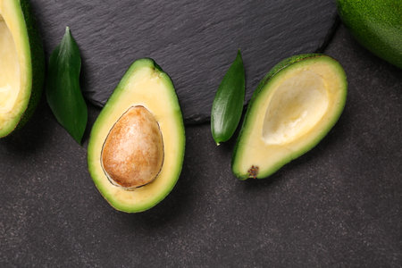 Halves of fresh ripe avocados and leaves on black background