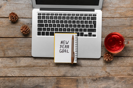 Notebook with text NEW YEAR GOAL, laptop and cup of tea on wooden backgroundの写真素材