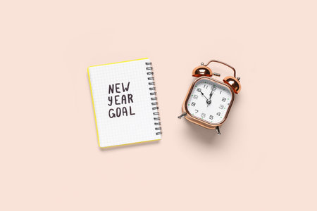 Notebook with text NEW YEAR GOAL and alarm clock on beige background