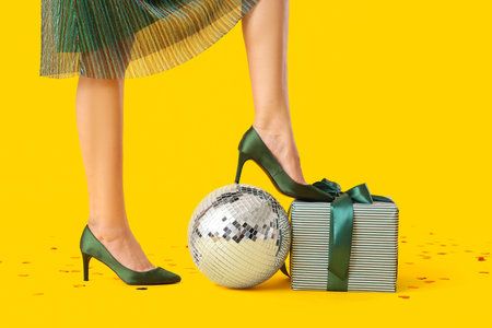 Beautiful young woman with disco ball and gift on yellow backgroundの写真素材
