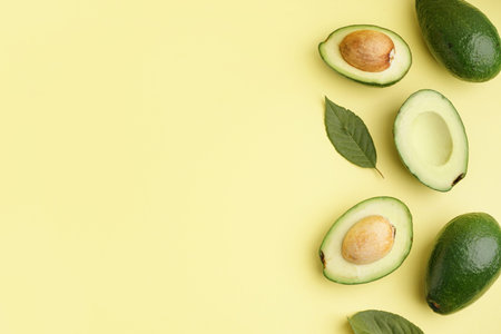 Fresh ripe avocados and leaves on yellow background